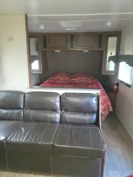 Comfortable RV rental interior featuring a dark brown sofa in the foreground and a cozy bed area with overhead storage in the back.. Heartland RVs Prowler 2018