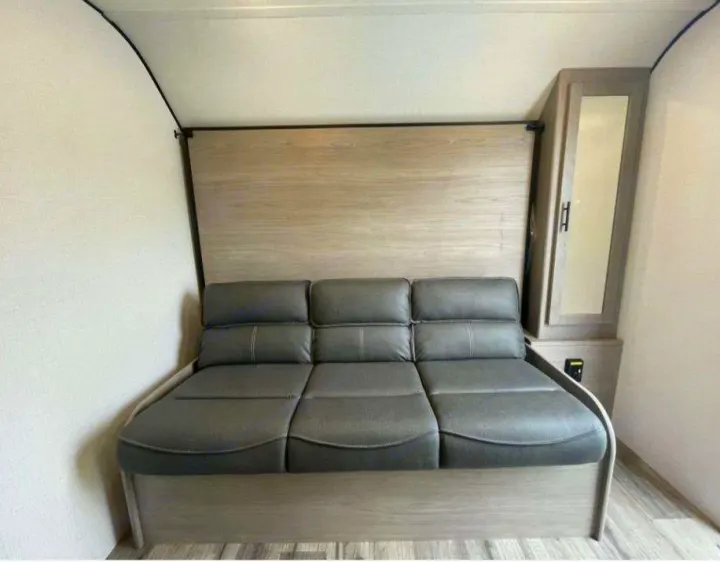 Compact RV rental interior showing a gray trifold sofa for seating & sleeping, with a mirrored cabinet & wood paneling.. Dutchmen Coleman 1905BH 2024