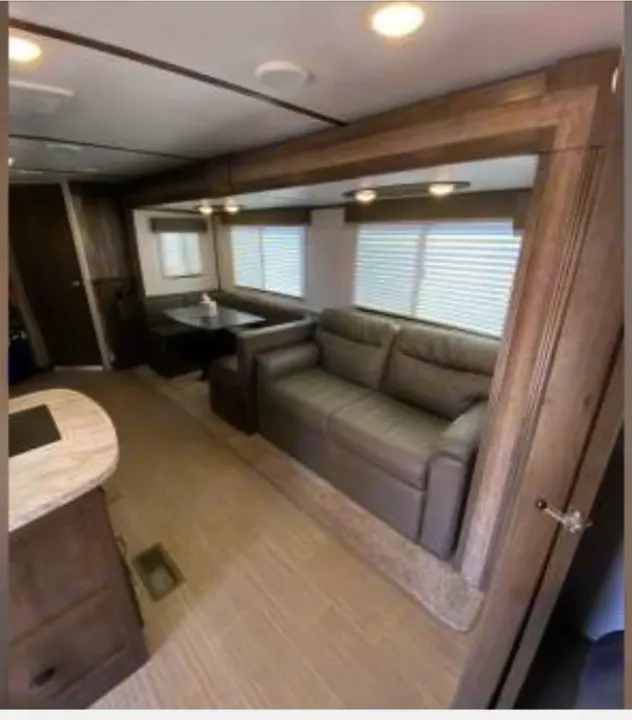 This RV rental's spacious interior features a modern living area with a gray sofa, dining booth, and kitchen counter for comfortable travel.. Keystone RV Passport SL 2021