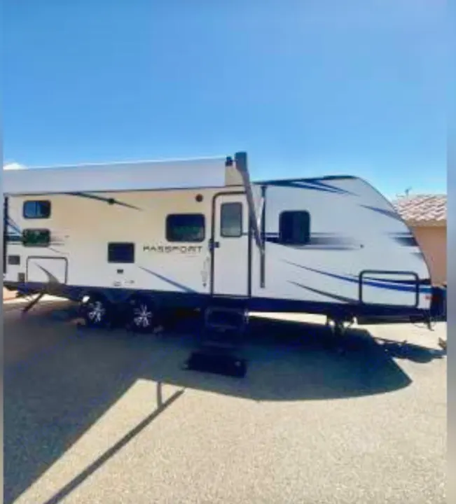 White Passport travel trailer with blue accents and extended awning, ideal for an rv rental. Parked on asphalt.. Keystone RV Passport SL 2021