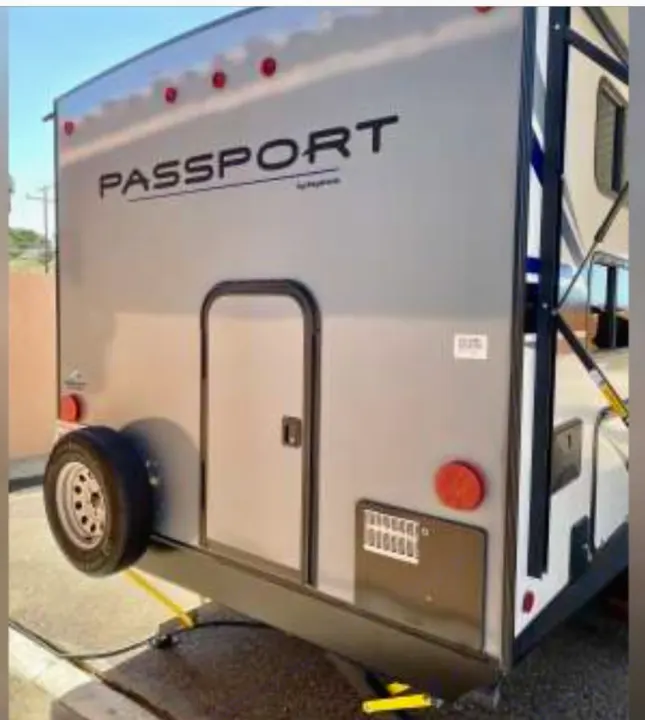 Explore a grey Passport travel trailer RV rental. Rear view highlighting the spare tire, access door, and utility vent.. Keystone RV Passport SL 2021