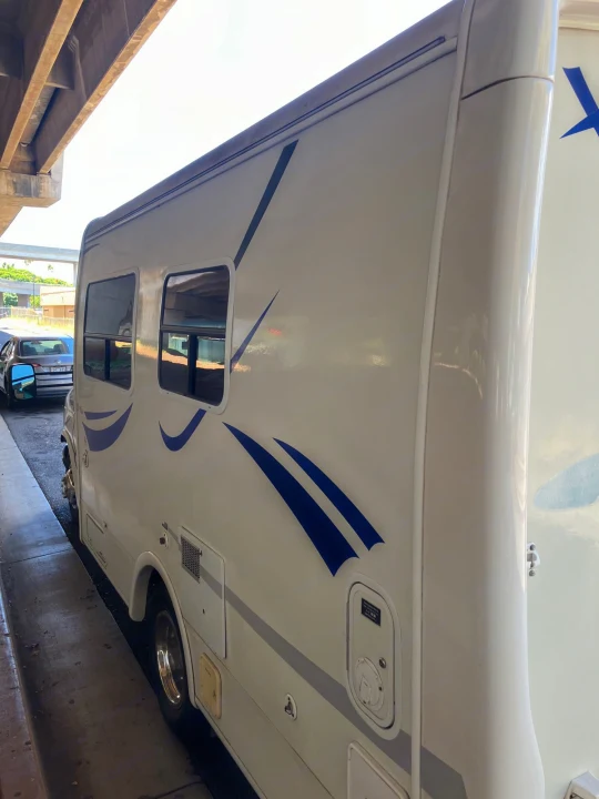 Side profile of an RV rental: a bright white motorhome with distinct blue graphics, parked under an overpass.. Ford Econoline 2004