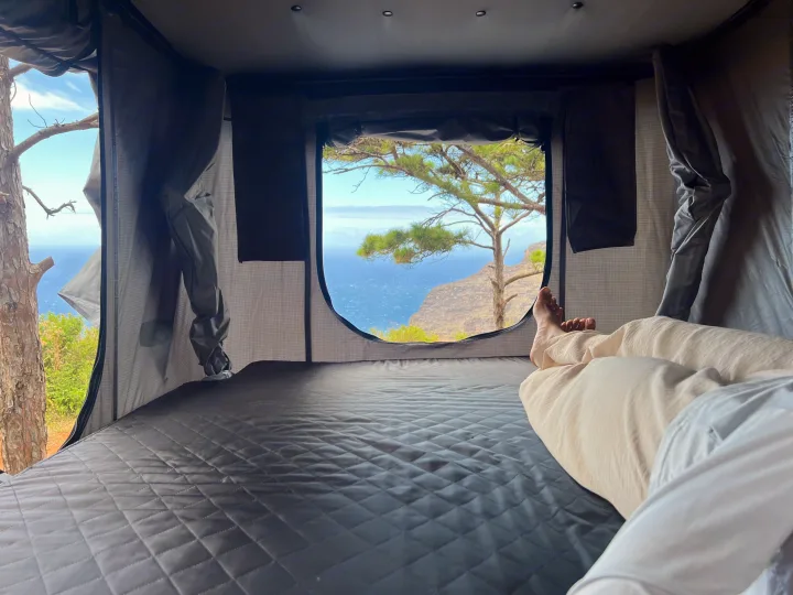 Relaxing in an RV rental's cozy rooftop tent, offering stunning ocean and cliff views. A perfect nature escape.. Jeep Wrangler 2008