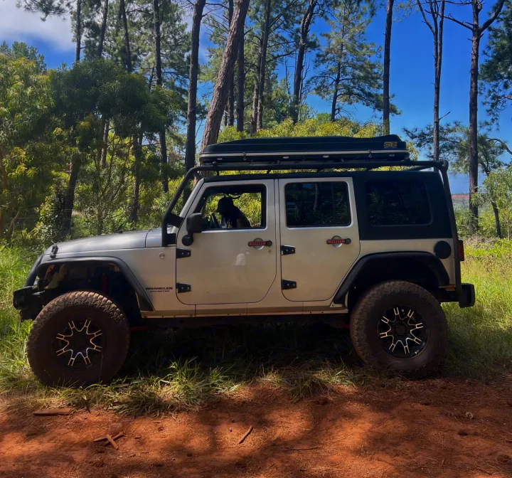 This silver Jeep Wrangler, perfect for an RV rental outdoor adventure, is parked on a forest trail with a dog in the driver's seat.. Jeep Wrangler 2008