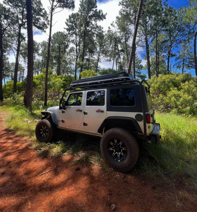 White Jeep Wrangler with rooftop tent on a dirt path in a pine forest, ideal for rv rental adventures and off-road trips.. Jeep Wrangler 2008