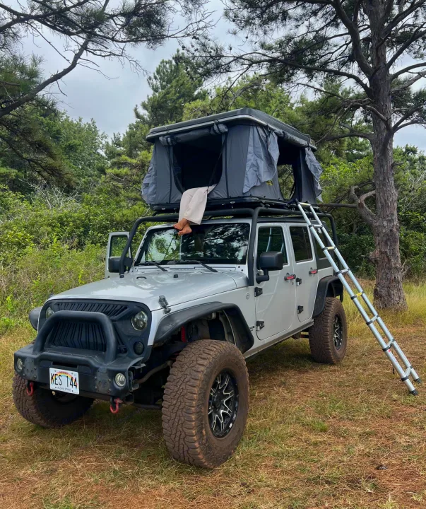 Unique RV rental: Silver Jeep with a rooftop tent and ladder. Bare feet dangle, enjoying an outdoor camping adventure.. Jeep Wrangler 2008