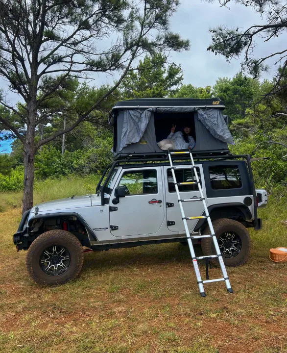 RV rental adventure awaits! A person relaxes in a rooftop tent on a Jeep Wrangler, ideal for outdoor camping escapades.. Jeep Wrangler 2008