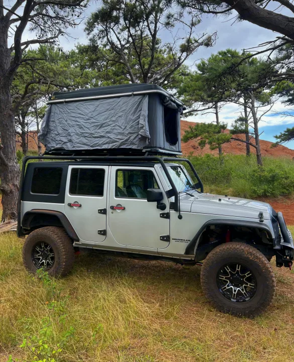 Silver Jeep Wrangler with rooftop tent, parked amidst pines & red hills. An RV rental option for overlanding.. Jeep Wrangler 2008