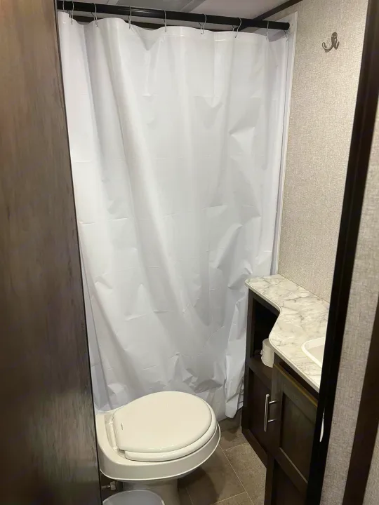 RV rental compact bathroom: white shower curtain, toilet, and vanity with sink. Essential comfort for your trip.. Dutchmen Coleman Lantern LT 2021