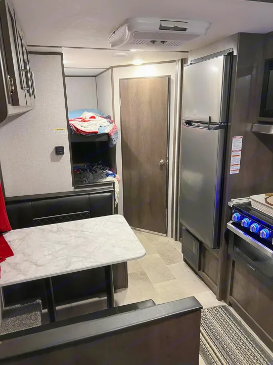 Full-featured RV rental interior: dining area, bunk beds, and kitchen with fridge and stove.. Dutchmen Coleman Lantern LT 2021