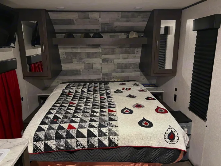 This cozy RV rental bedroom features a unique quilt, overhead cabinets, and blackout blinds for your comfort.. Dutchmen Coleman Lantern LT 2021
