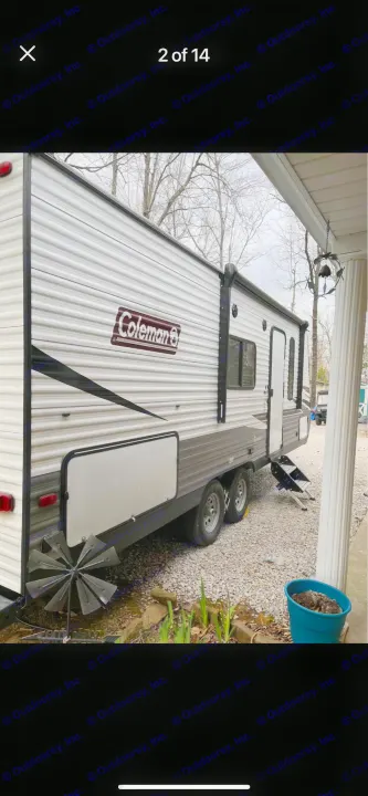Side view of a Coleman RV rental, a white and gray travel trailer, parked on gravel next to a porch.. Dutchmen Coleman Lantern LT 2021