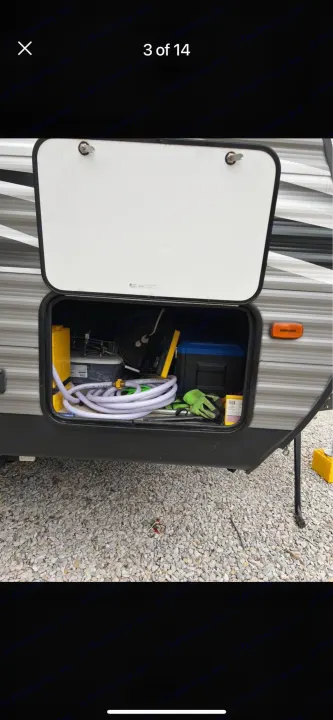 Open RV rental storage bay reveals coiled hoses, yellow leveling blocks, and essential camping gear.. Dutchmen Coleman Lantern LT 2021
