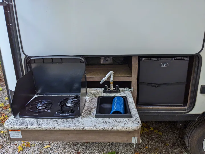 RV rental outdoor kitchen setup: a two-burner stove, small sink with flexible faucet, and mini-fridge for convenient camping.. Keystone RV Passport Ultra Lite 2018