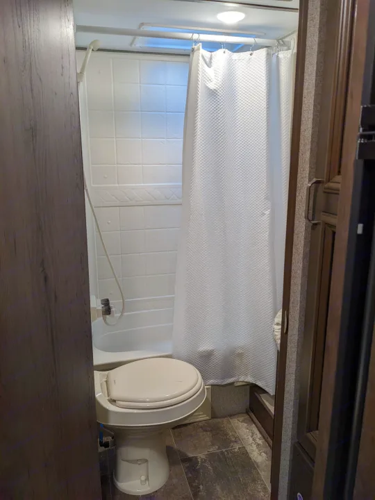 Compact RV rental bathroom: white toilet, small tub/shower, and shower curtain. Functional for travel.. Keystone RV Passport Ultra Lite 2018