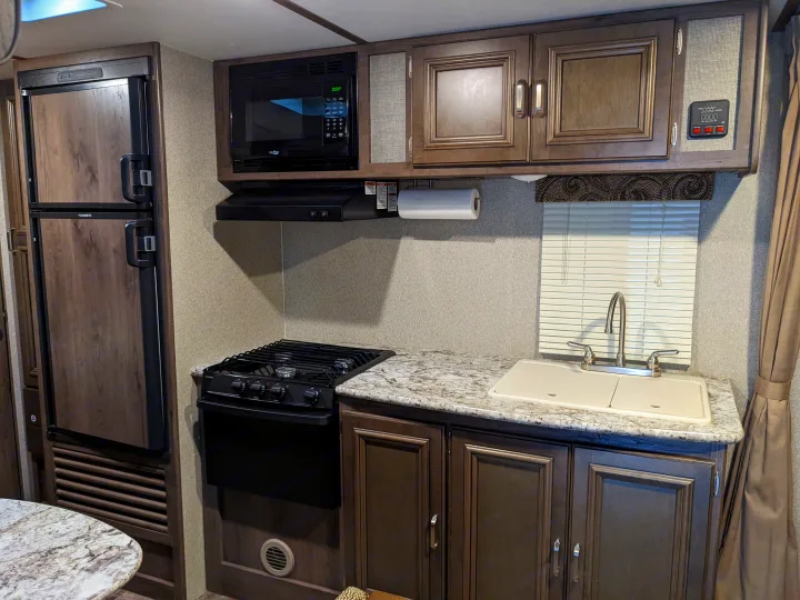 Inside this RV rental, find a functional kitchen with a fridge, microwave, stove, sink, and granite-look counters.. Keystone RV Passport Ultra Lite 2018