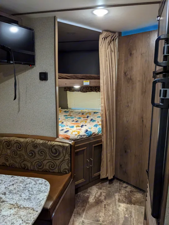 This cozy RV rental interior features a dinette, TV, and bunk beds, offering comfortable living and sleeping for travel.. Keystone RV Passport Ultra Lite 2018