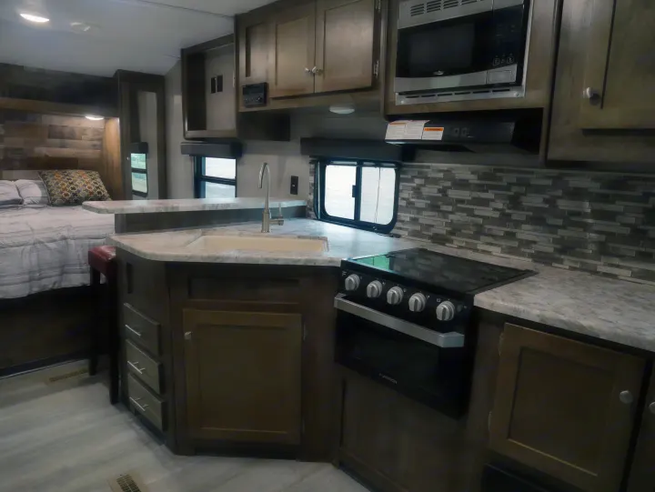 Spacious RV rental interior with a modern kitchen, built-in appliances, and a cozy bedroom area. Great for travel.. Dutchmen Aspen Trail 2020