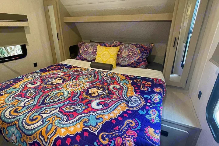Vibrant RV rental bedroom: a cozy bed with a colorful, patterned quilt and pillows, plus built-in storage.. Forest River Salem Cruise Lite 2023