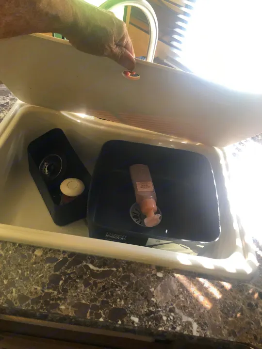 Person lifts RV rental sink cover, exposing a compact Joseph Joseph wash basin with soap on a dark counter.. Keystone RV Springdale 2017