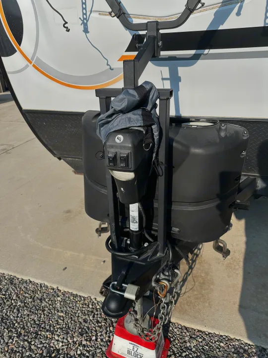 Close-up of an RV rental's front tongue, showing hitch, electric jack, and propane tanks, secured with chains and block.. Forest River GeoPro 2022