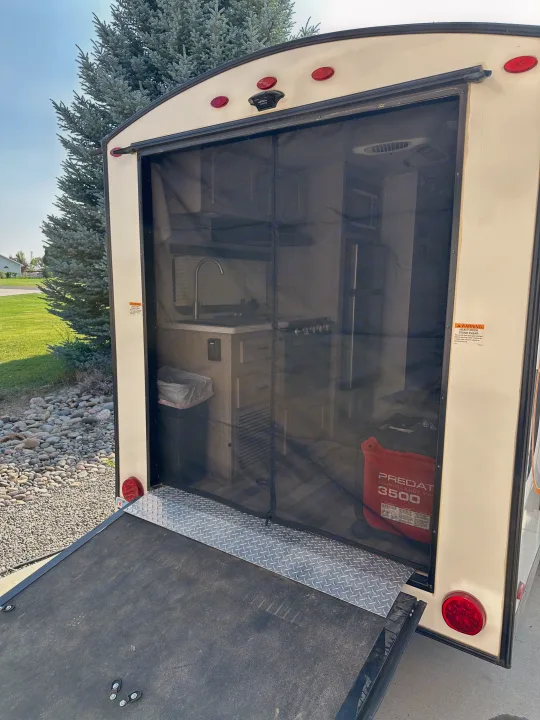 RV rental's rear ramp is down, revealing a mesh screen door to the kitchen interior and a PREDATOR 3500 generator.. Forest River GeoPro 2022