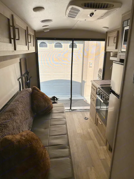 Spacious toy hauler RV rental interior with a comfortable sofa, kitchen, and large screened rear door open to the outside.. Forest River GeoPro 2022