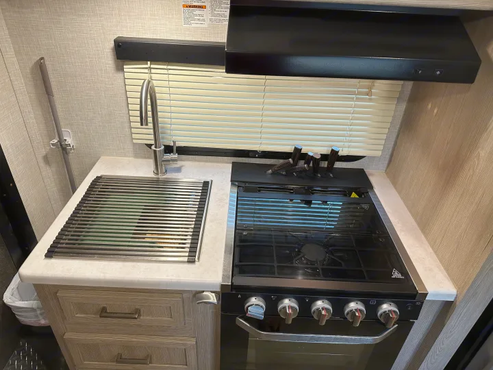 Compact RV rental kitchen featuring a sink, stove, oven, range hood, and integrated knife block.. Forest River GeoPro 2022