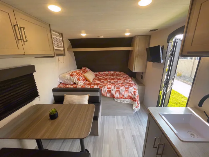 Clean RV rental interior with a comfy bed, dining area, kitchen, and AC unit. Ready for adventure!. Keystone Springdale 1800BH 2024