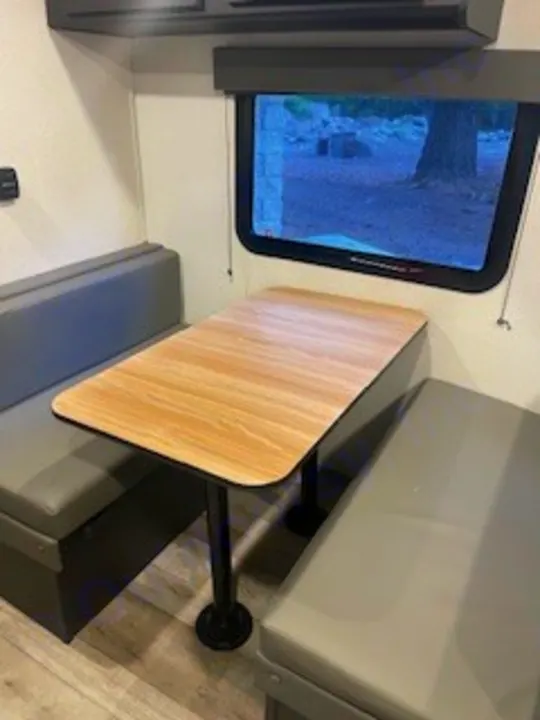 RV rental dinette with gray cushioned benches, a wood table, and a window view, perfect for camping trips.. Keystone RV Springdale 2022