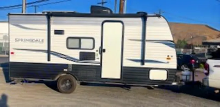 A white & black Springdale travel trailer, perfect for an rv rental, is parked outdoors with an open door.. Keystone RV Springdale 2022