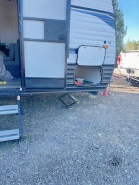 An rv rental travel trailer, with open door, extended steps, and storage bays accessible, parked on a gravel lot.. Keystone RV Springdale 2022