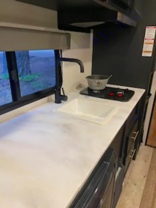 RV rental kitchen: modern sink, black faucet, 2-burner stove with pot, and large window offering outdoor views.. Keystone RV Springdale 2022