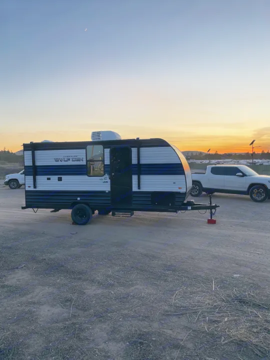 A Cherokee Wolf Den travel trailer (RV rental) and Rivian truck parked at sunset, perfect for camping adventures.. Forest River Wolf Den 16EV 2024