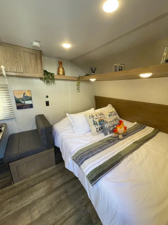 Cozy RV rental bedroom featuring a comfortable bed with camping-themed pillows, a small dinette, and overhead storage.. Forest River Wolf Den 16EV 2024