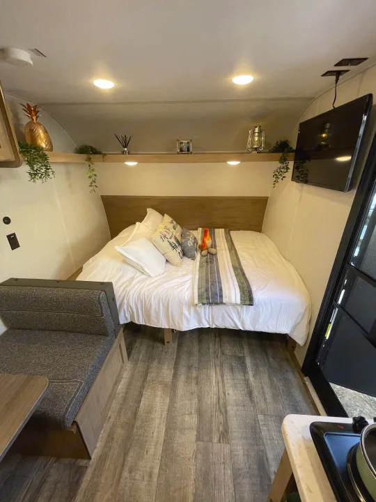 Inside a modern RV rental: a compact living space featuring a comfortable bed, dinette, TV, and partial kitchen area.. Forest River Wolf Den 16EV 2024