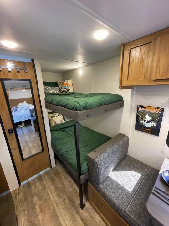 Cozy RV rental bunk beds with camping-themed pillows & green bedding, plus a comfy dinette & wood-look floor.. Forest River Wolf Den 16EV 2024