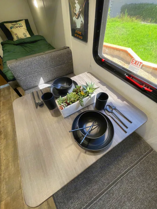 RV rental: Cozy interior with a modern dinette setup, including black dishes, succulent decor, and a comfy bed area.. Forest River Wolf Den 16EV 2024