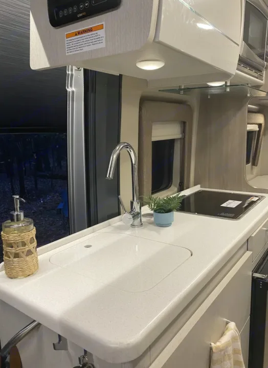 Inside a modern RV rental: sleek kitchen with sink, stovetop, & outdoor view. Compact amenities for your next adventure.. Thor Tellaro 2022