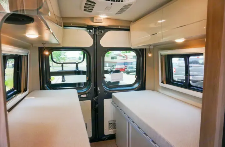 Spacious RV rental interior with dual single beds, overhead storage, and large rear windows for comfort and views.. Thor Tellaro 2022