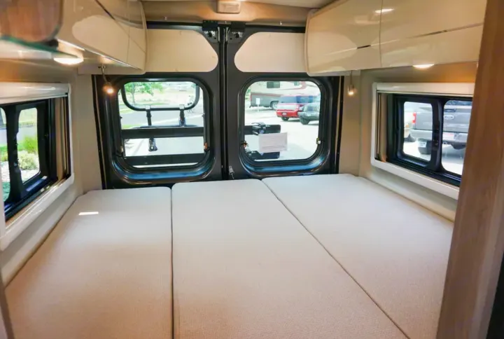 RV rental camper van interior. Spacious sleeping area with three mattress sections, large rear windows, and overhead storage.. Thor Tellaro 2022