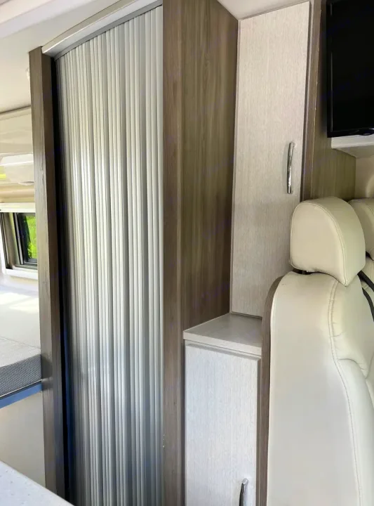 Compact RV rental interior featuring modern wood cabinetry, a roll-up door, and storage by the seat.. Thor Tellaro 2022