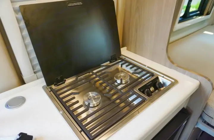 Inside an RV rental: a compact stainless steel 2-burner gas cooktop with an open cover built into a white countertop.. Thor Tellaro 2022