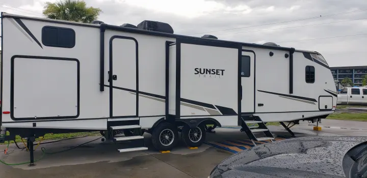 White "Sunset Trail" RV rental travel trailer set up at a site with slides extended, steps down, and utility connections.. Keystone Sunset Trail 2022