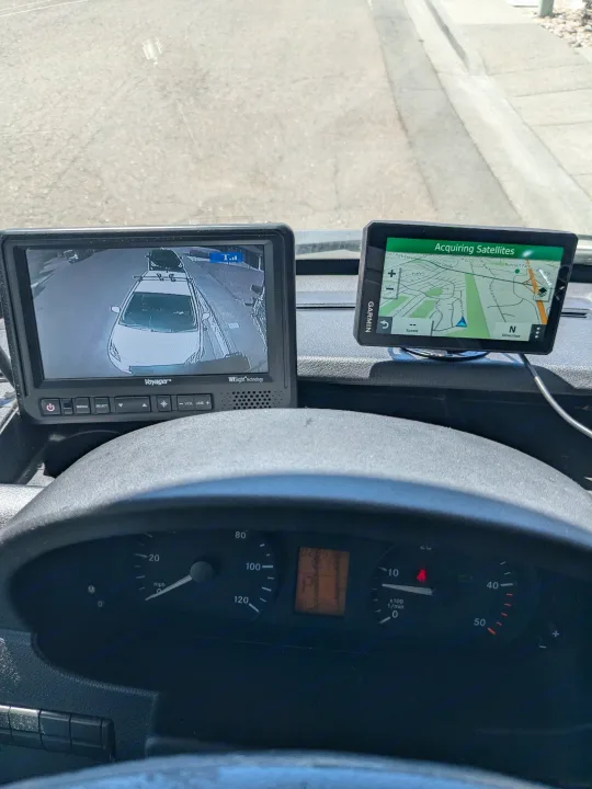 RV rental dashboard showing a Voyager rearview camera monitor with a car behind, and a Garmin GPS screen for navigation.. Forester Forester Motorhome 2019