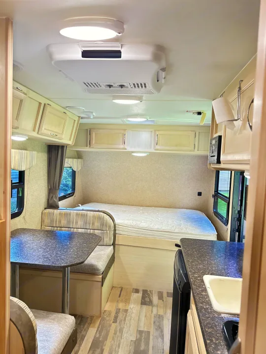 Bright rv rental interior featuring a dining table, comfortable bed, kitchen sink, and overhead storage cabinets.. Minnie Micro Minnie 2018