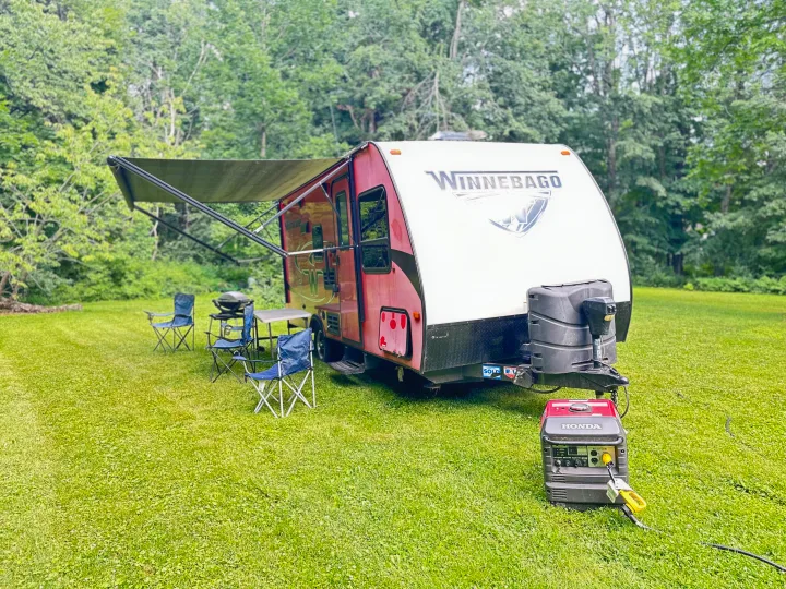 This Winnebago RV rental sits on a lush lawn with an extended awning, camp chairs, grill, and Honda generator, ready for outdoor adventure.. Minnie Micro Minnie 2018