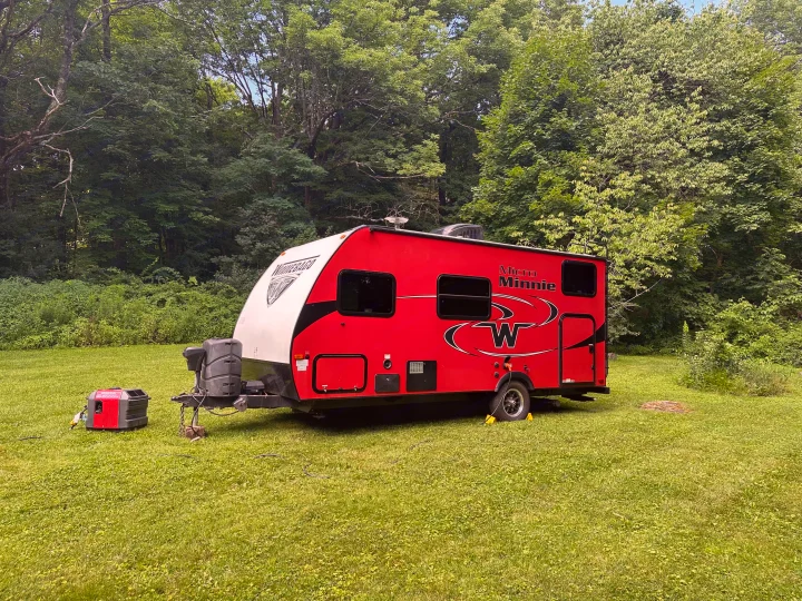 Red Winnebago Micro Minnie rv rental parked in a green field with a generator. Lush trees in background for camping adventures.. Minnie Micro Minnie 2018