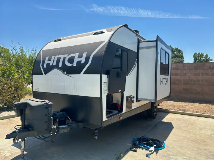 A clean white and black "HITCH" travel trailer, perfect for an RV rental adventure, parked on concrete under a blue sky.. Cruiser RV Hitch 2022