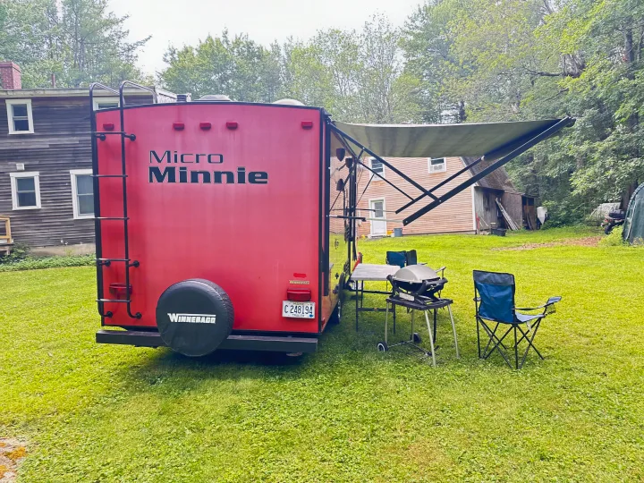 Red Winnebago Micro Minnie RV rental with extended awning, grill, and chairs set up in a grassy yard.. Minnie Micro Minnie 2018
